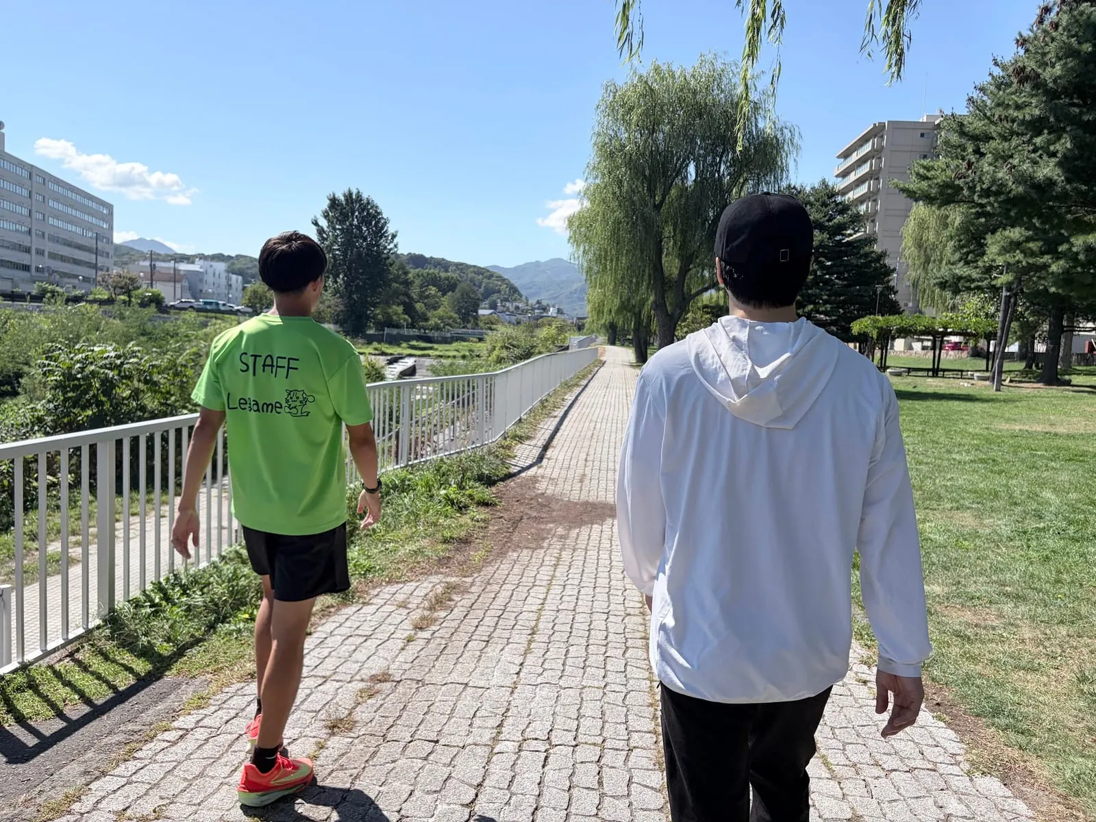 川沿いの遊歩道を歩き出すスタッフと会員（後ろ姿）