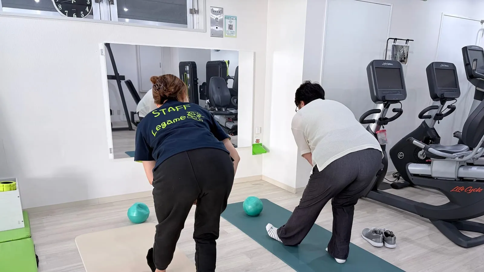 スタッフと会員が並んで前屈の動き（後ろ姿）